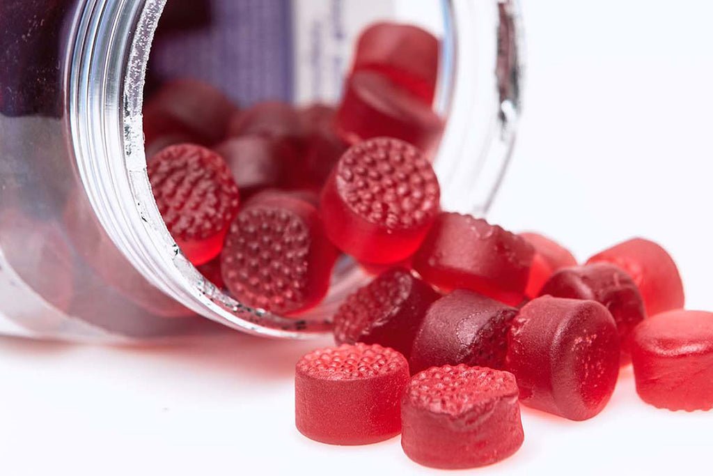 Offen liegender Nahrungsergänzungsmittel-Behälter, wo rote Vitamin-Gummies auf den Tisch kullern