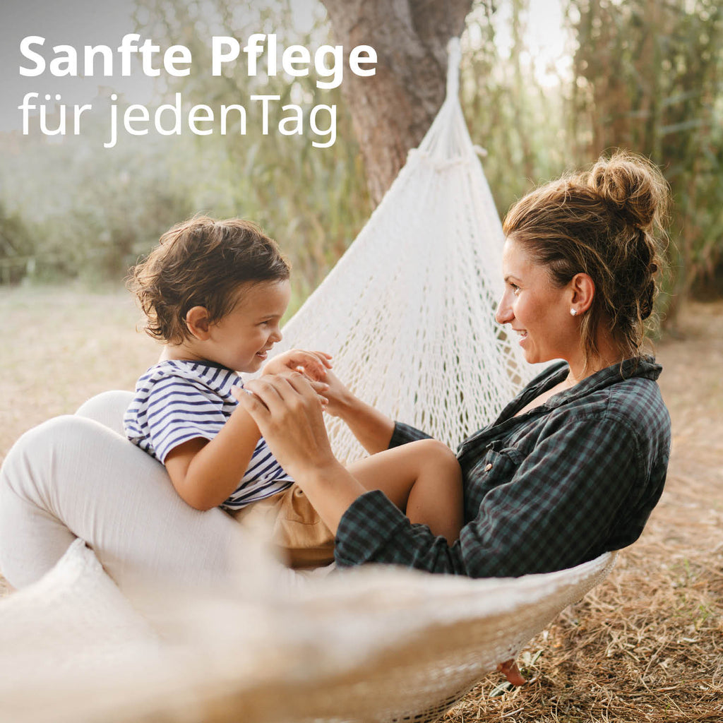 Eine Mutter mit ihrem Kind sitzen in einer Hängematte und lächeln sich an. Text: Sanfte Pflege für jeden Tag